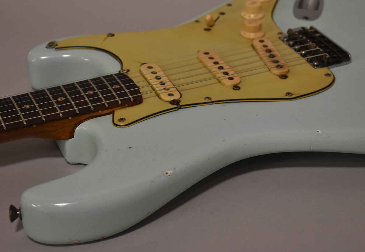 Light blue guitar body with a cream pickguard and pickups, showing significant wear and chips in the finish.