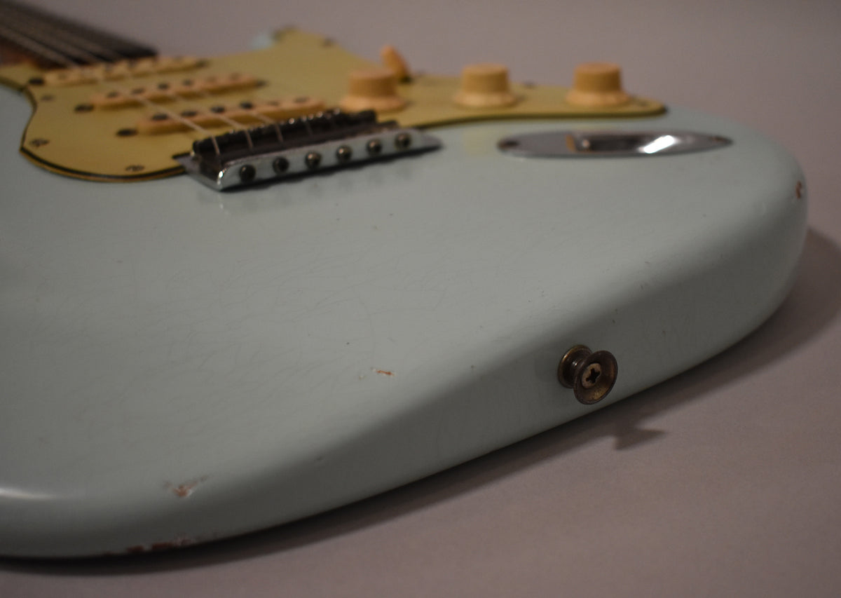 Close-up of the guitar's lower body, showing the aged sonic blue finish with fine checking, a worn output jack, and a few chips.