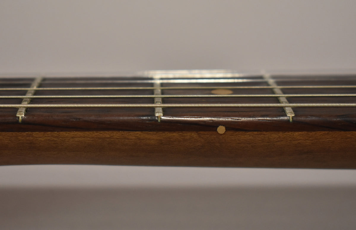 Close-up of the guitar neck from the side, showing the dark rosewood fretboard with light dot inlays and the worn, dark wood neck.