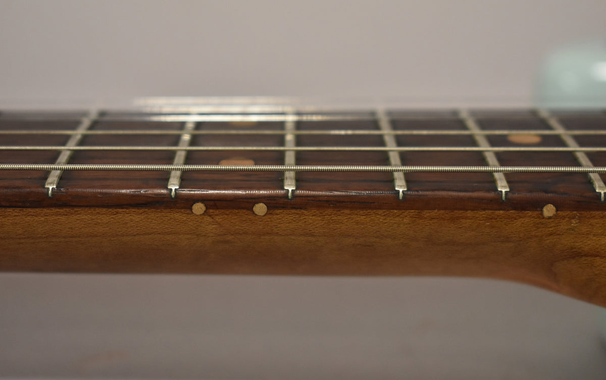 Close-up of the guitar's dark rosewood fretboard and light brown neck, showing side dot markers and light wear on the frets.