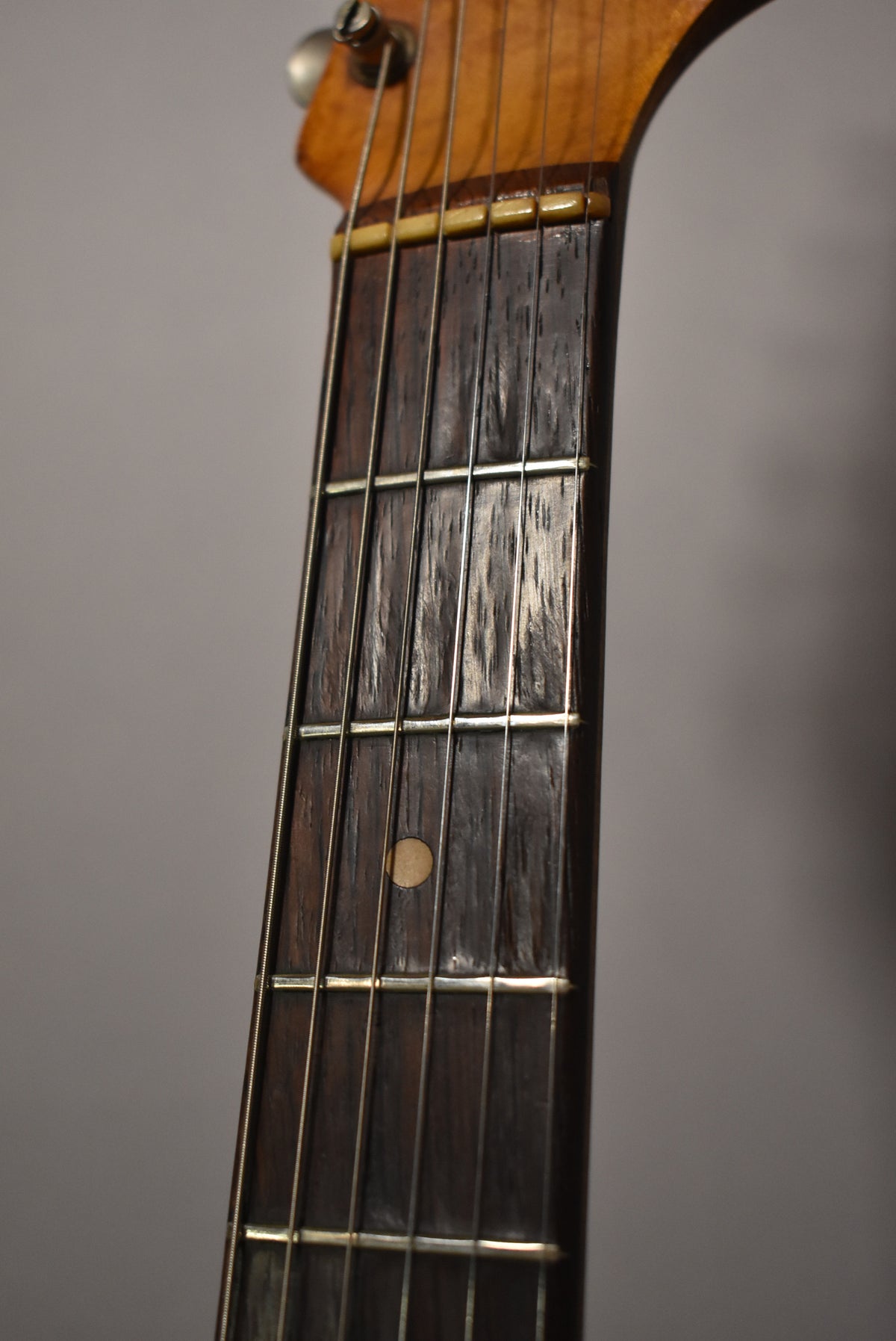 Close-up of the dark rosewood fretboard and frets, showing a light circular inlay at the 7th fret and a worn, ambered nut.