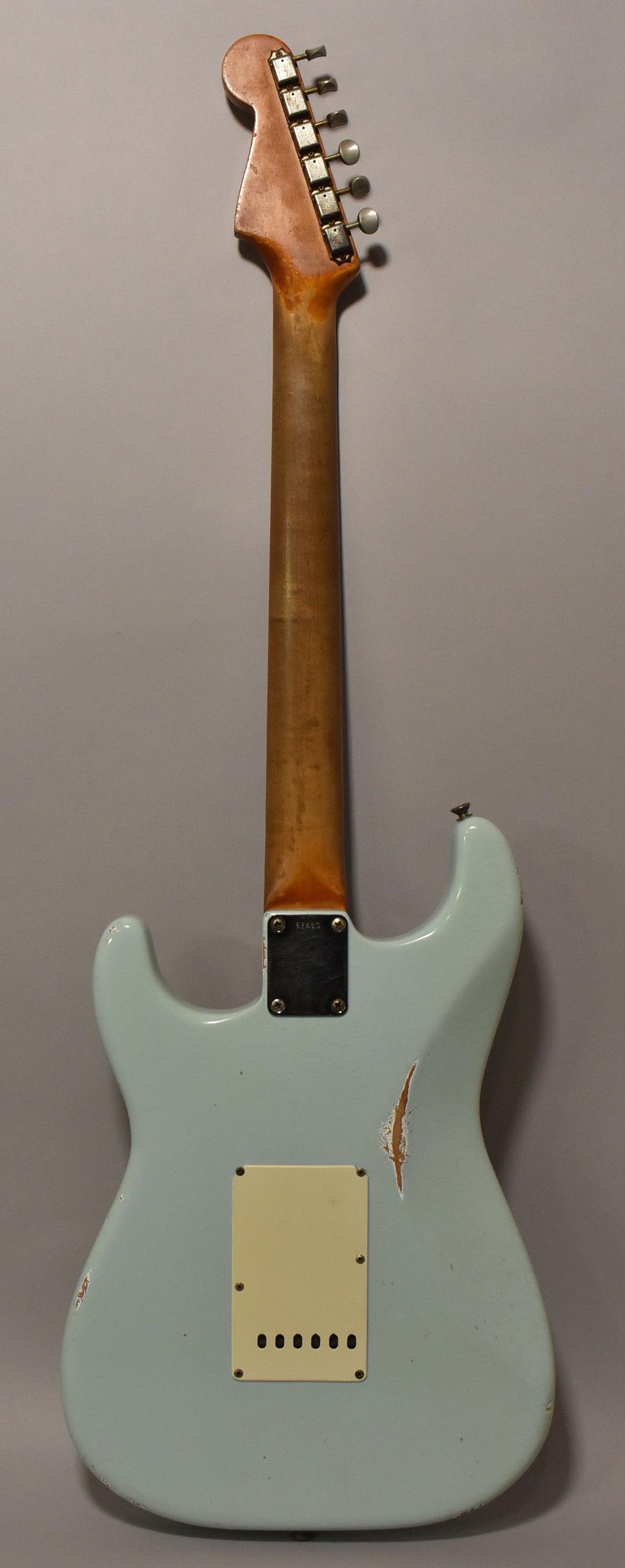 Rear view of a light blue Stratocaster with a worn, aged finish, showing a large chip on the upper bout and a cream tremolo cover.