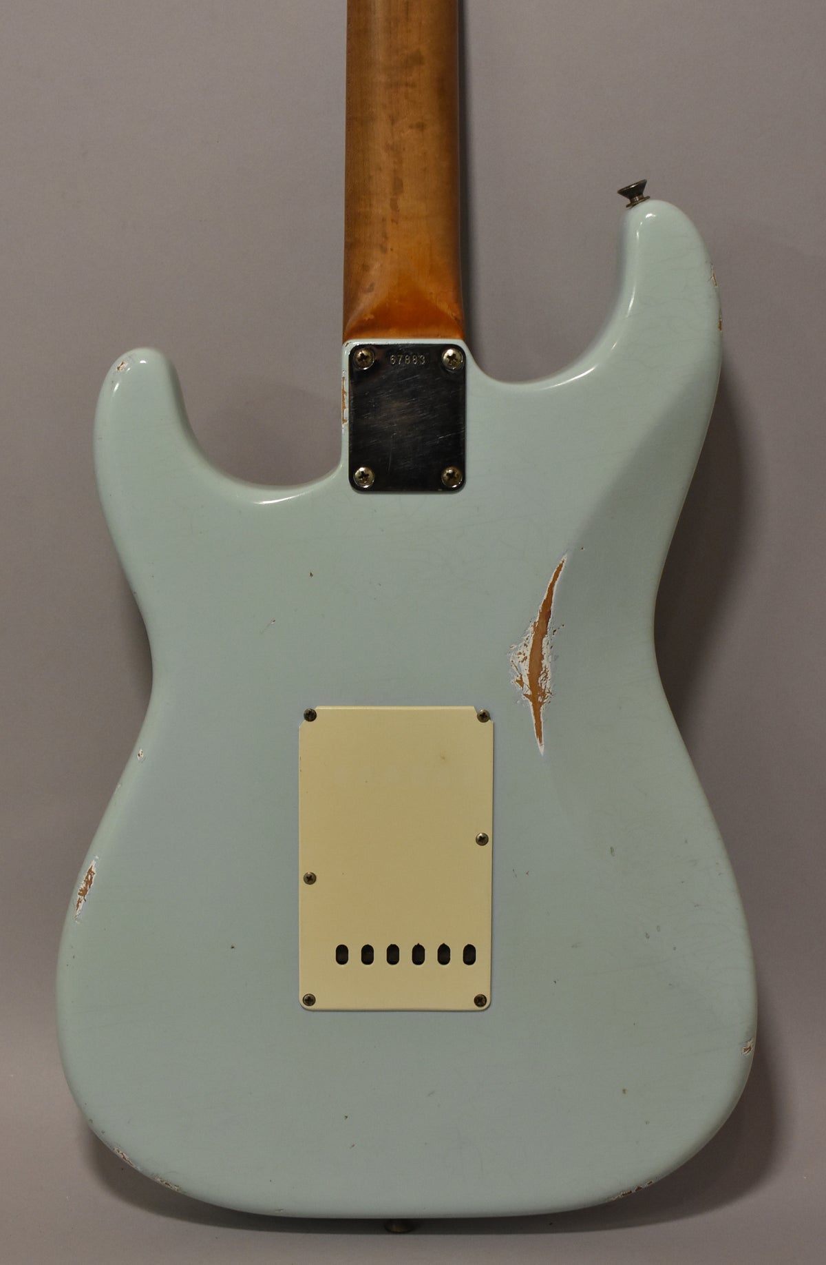 The back of a light blue guitar body with a cream tremolo cover, a worn neck plate, and significant paint chips revealing wood.