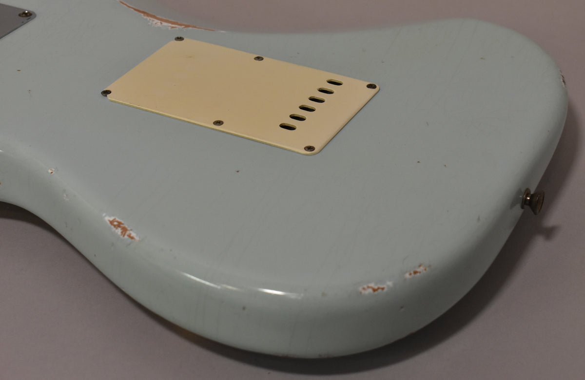 The back of a light blue guitar body, showing a cream tremolo cover, heavy finish wear, and a strap button.