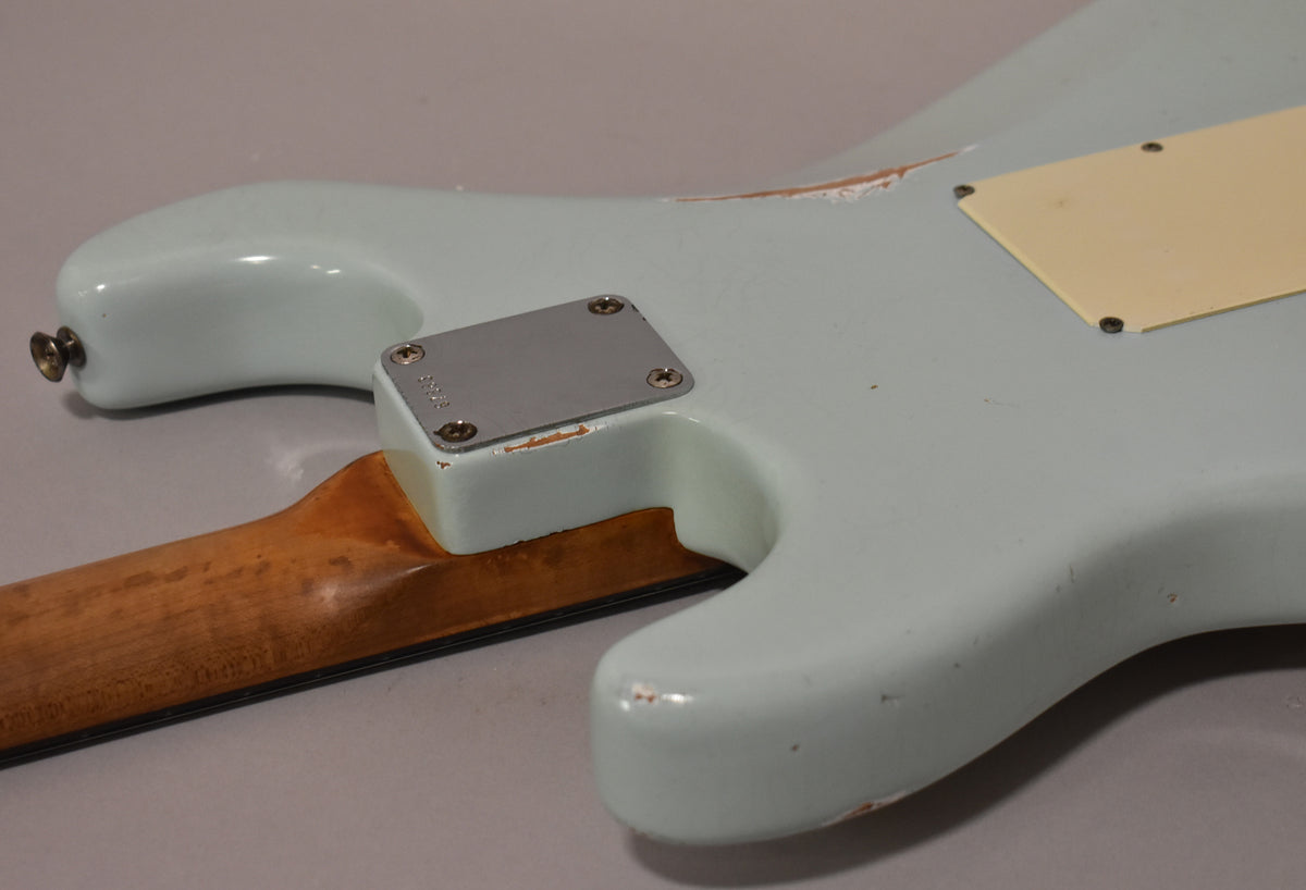 The back of a light blue guitar body, showing the neck plate, output jack, tremolo cover, and significant paint wear.