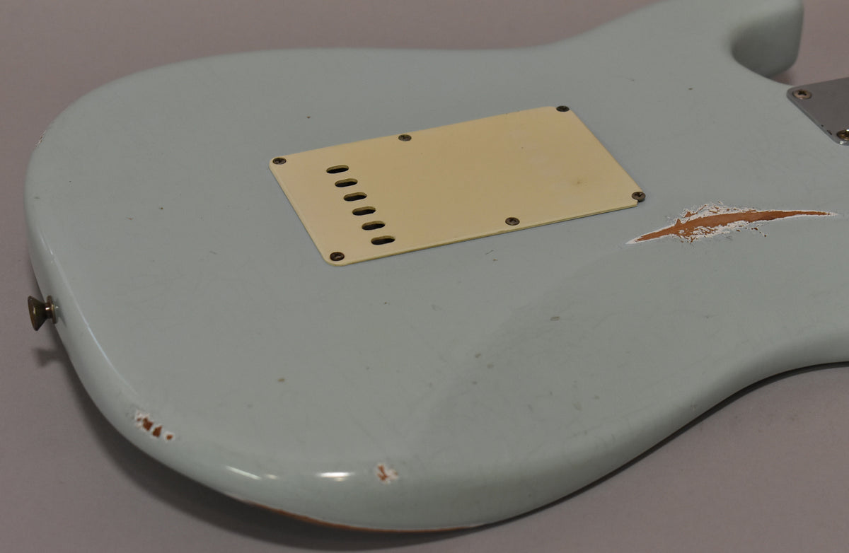 The back of a light blue guitar body, showing a cream tremolo cover and significant paint wear revealing wood.