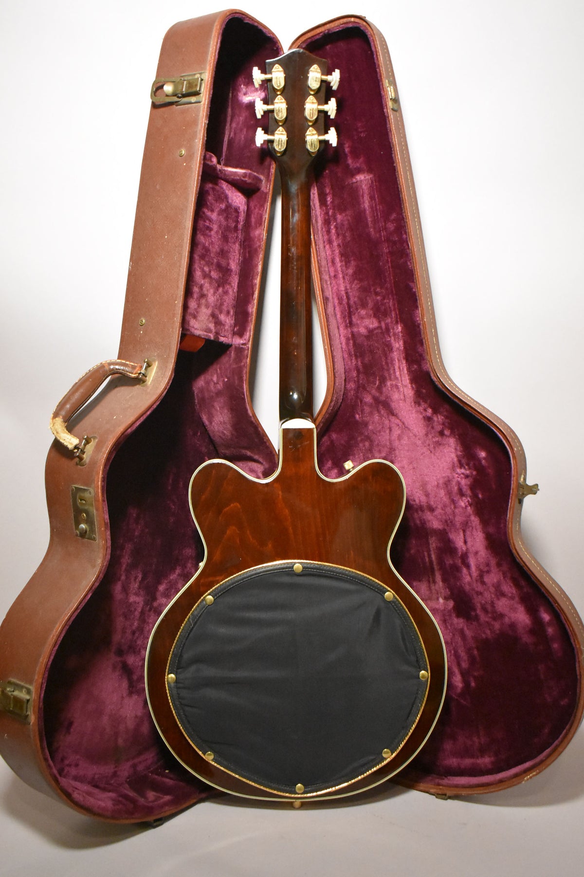 The guitar's dark walnut back and neck are visible, with a black circular pad covering the back, resting in a brown case with purple velvet lining.
