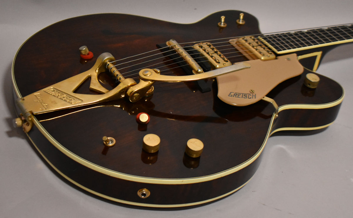 Close-up of the dark walnut guitar body, showing the gold Bigsby tremolo, pickguard, two gold pickups, and three gold control knobs.