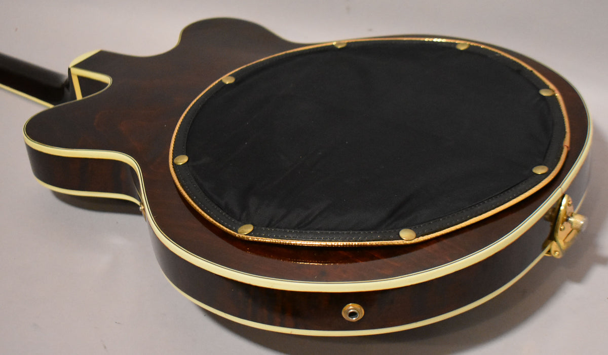The guitar's dark walnut back and sides are visible, with a black padded back pad secured by brass snaps.