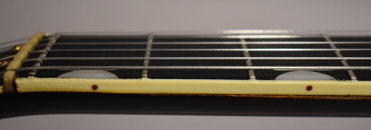 Close-up of the dark fretboard and frets, with cream binding showing red side dots and two half-moon inlays.