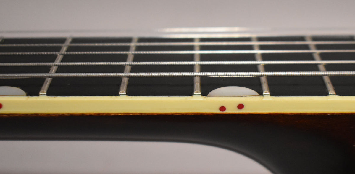 Close-up of the dark fretboard and frets, showing cream binding with two red side dots and a half-moon inlay.