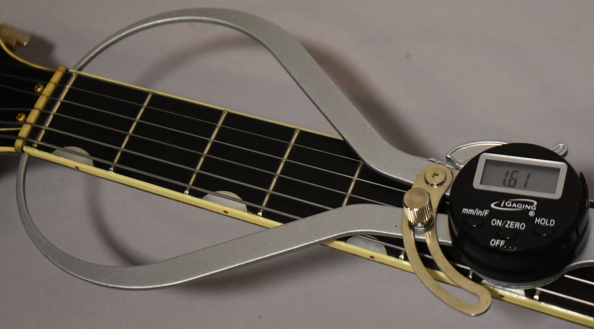 A close-up of the guitar's dark fretboard with white binding, showing a digital string action gauge reading 1.61mm.