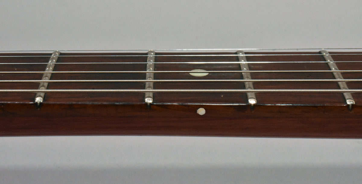Close-up of a guitar fretboard with six strings, frets, and two circular inlays, one on the fretboard and one on the side.