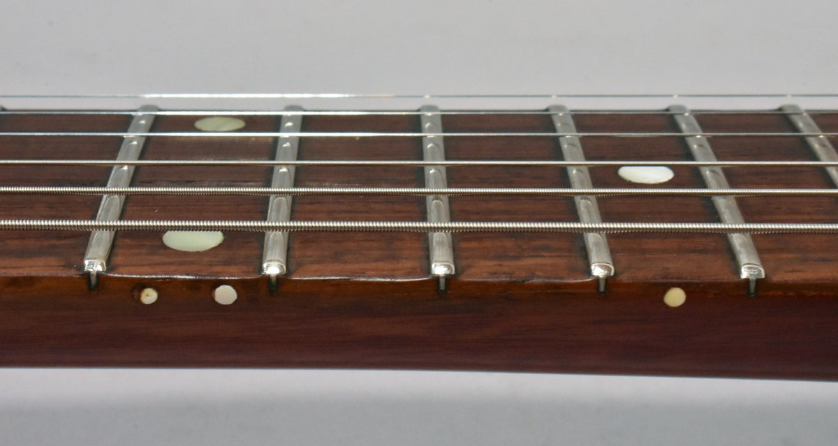 Close-up of a guitar fretboard with strings, frets, and mother-of-pearl inlays on the fretboard and side.