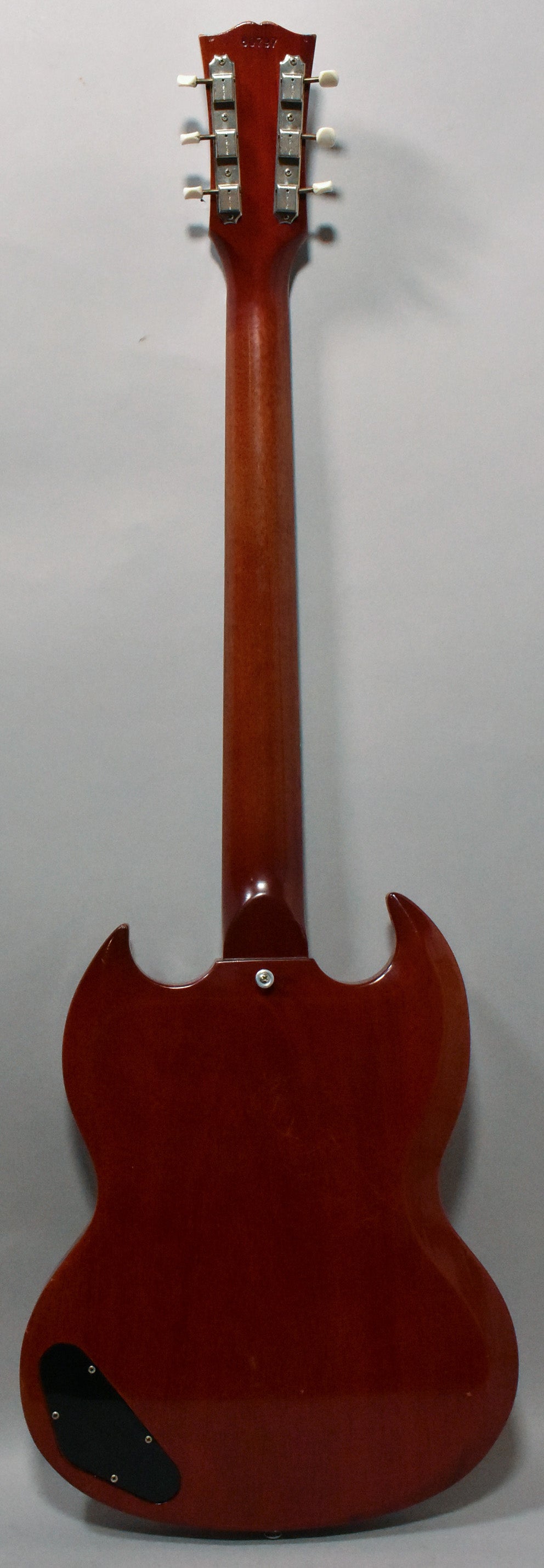 The back of a cherry red SG, showing the neck, headstock with six white-button tuners, and a black control cavity cover.