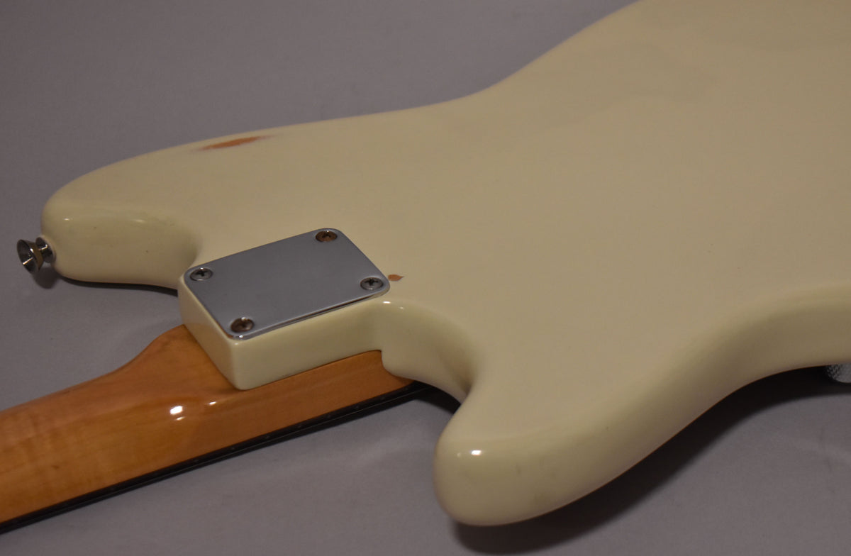 The back of a white refinished guitar body, showing the neck plate, strap button, and a chip revealing wood.