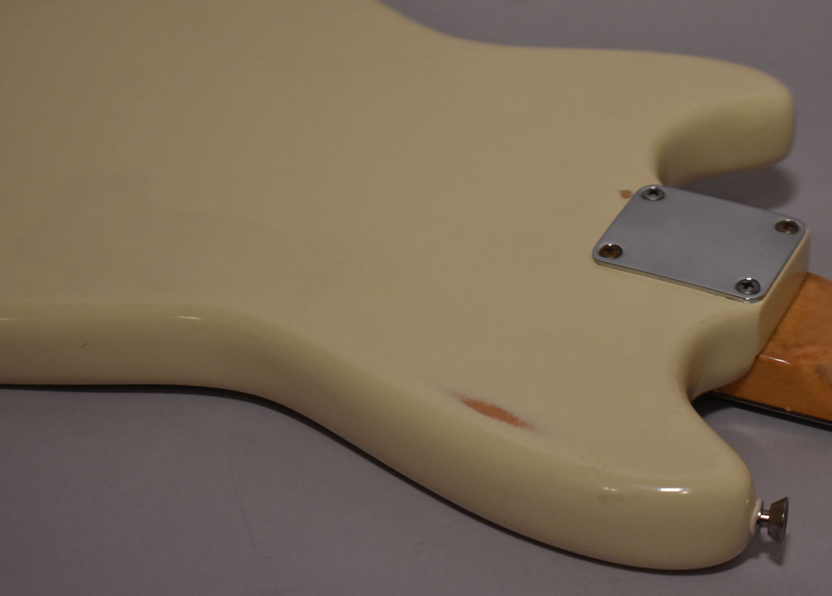 The back of the white refinished guitar body shows a chrome neck plate, a strap button, and a chip revealing wood.