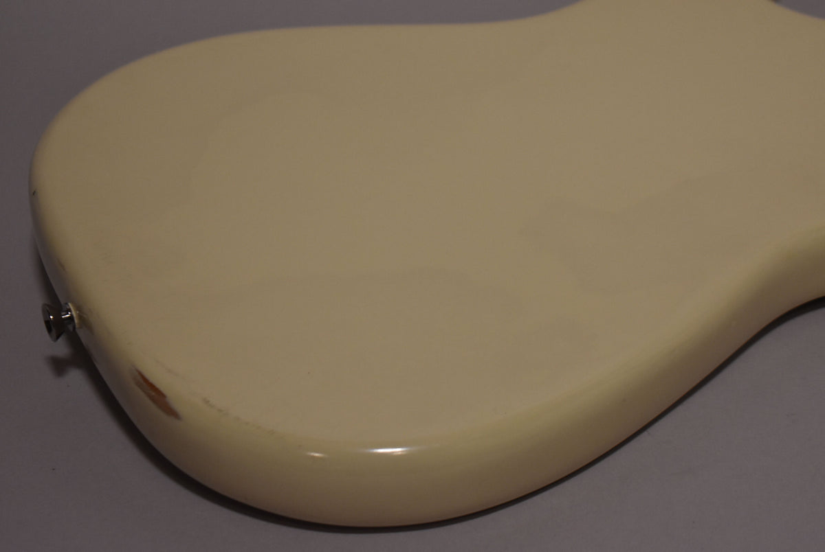 The guitar's white refinished body is shown from the back, with a chip revealing wood near the input jack.