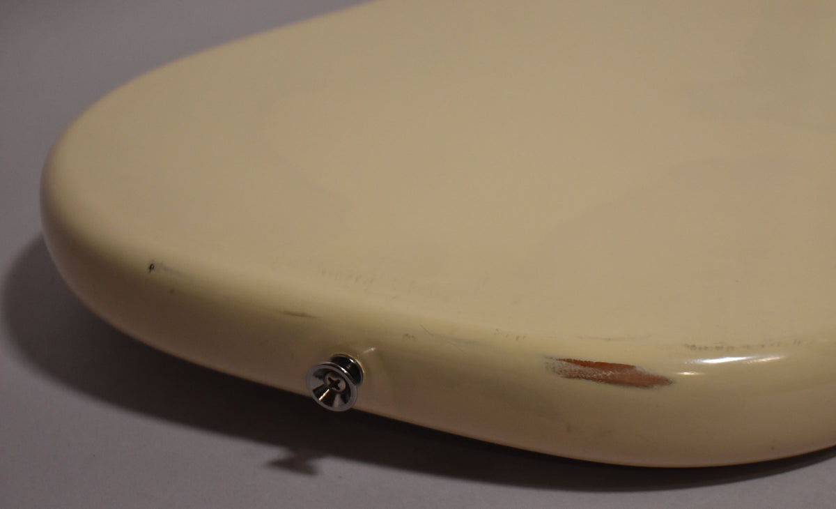 Close-up of the guitar's lower bout, showing the cream refinish with a large chip revealing wood and a chrome strap button.