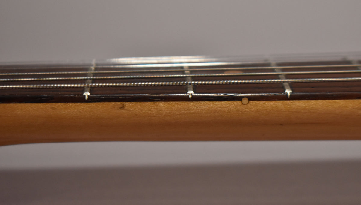Close-up of the guitar's dark fretboard and light maple neck, showing four strings, three fret markers, and a small ding on the neck.