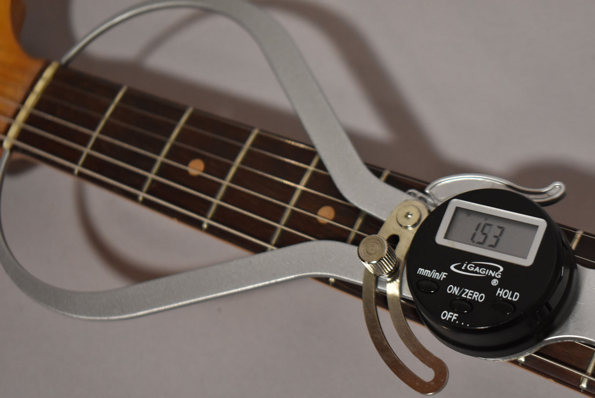 A digital fret height gauge shows a reading of 1.53mm, clamped over the dark rosewood fretboard with light dot inlays and metal frets.