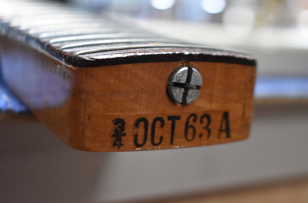 Close-up of the guitar neck heel, showing a large flathead screw and "OCT 63 A" stamped in black on the light brown wood.