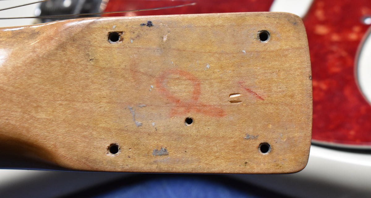 Close-up of the guitar's worn, light brown headstock back, showing four tuner screw holes and a red "Q" marking.