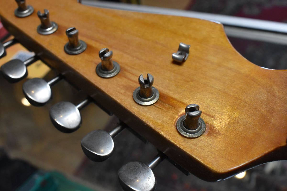 Close-up of the guitar's light brown headstock, showing six tarnished silver tuning pegs and a metal string tree.