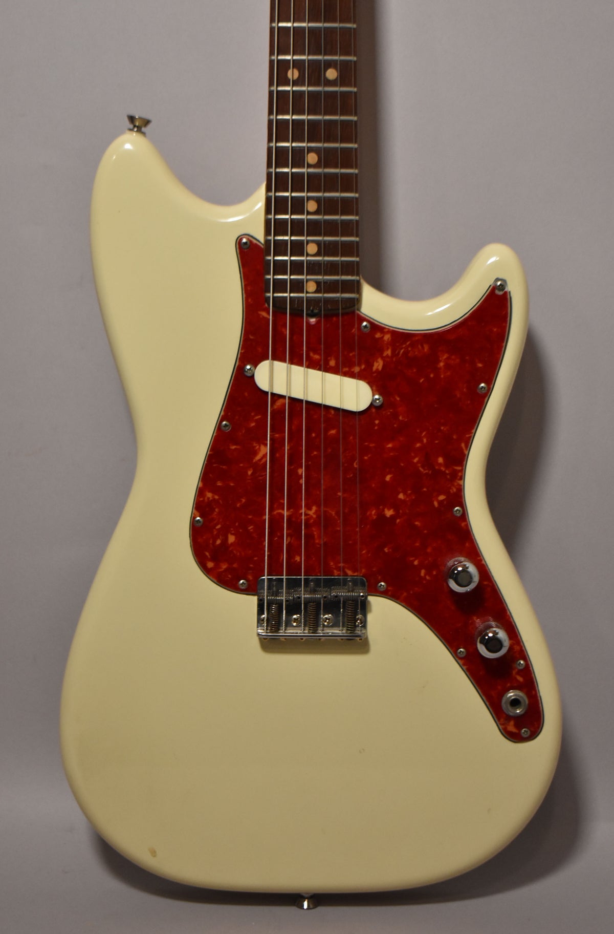 Full front view of a white electric guitar with a red tortoiseshell pickguard, single white pickup, chrome bridge, and two chrome knobs.
