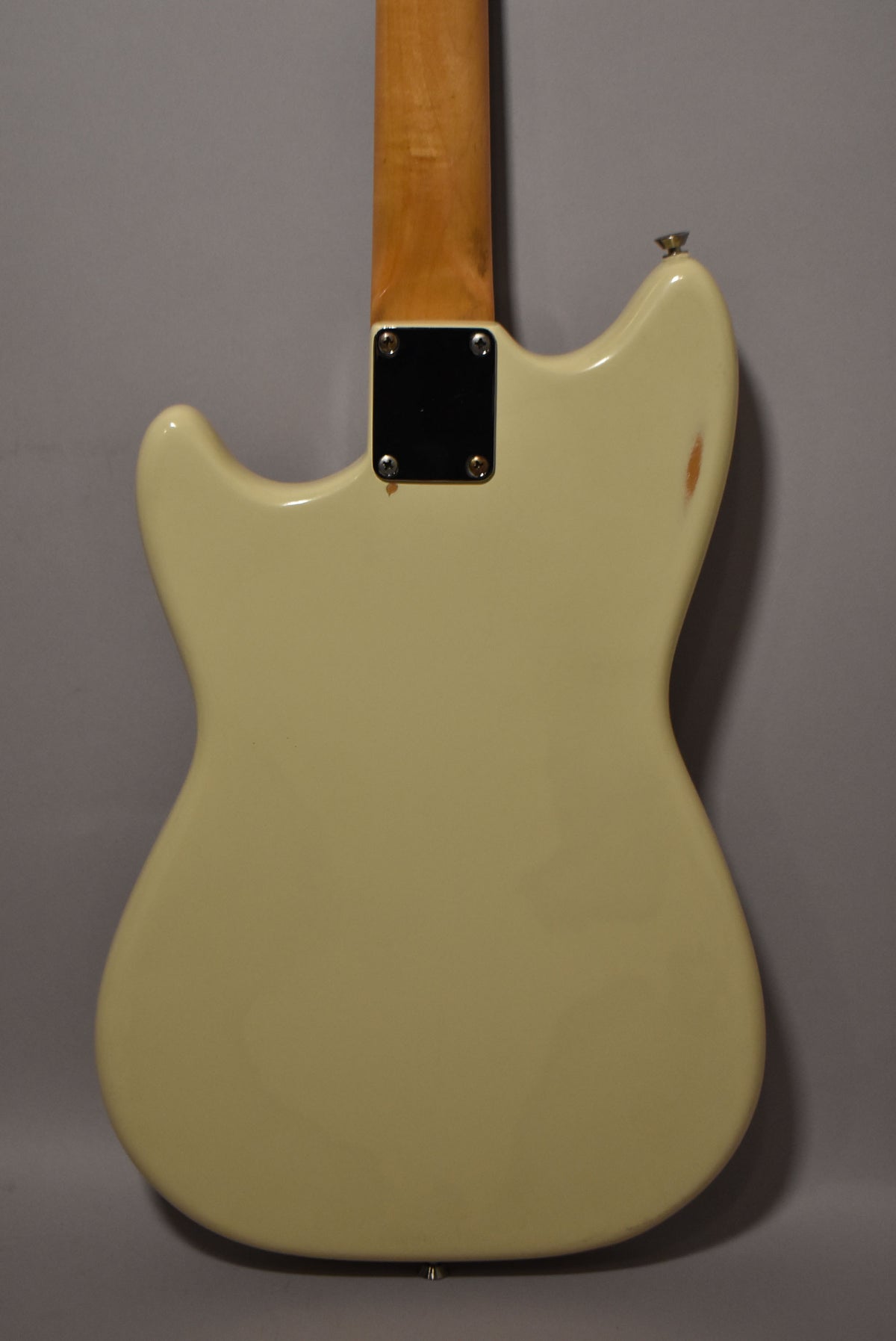 The back of a white electric guitar, showing the neck joint, a strap button, and a chip in the finish on the upper bout.