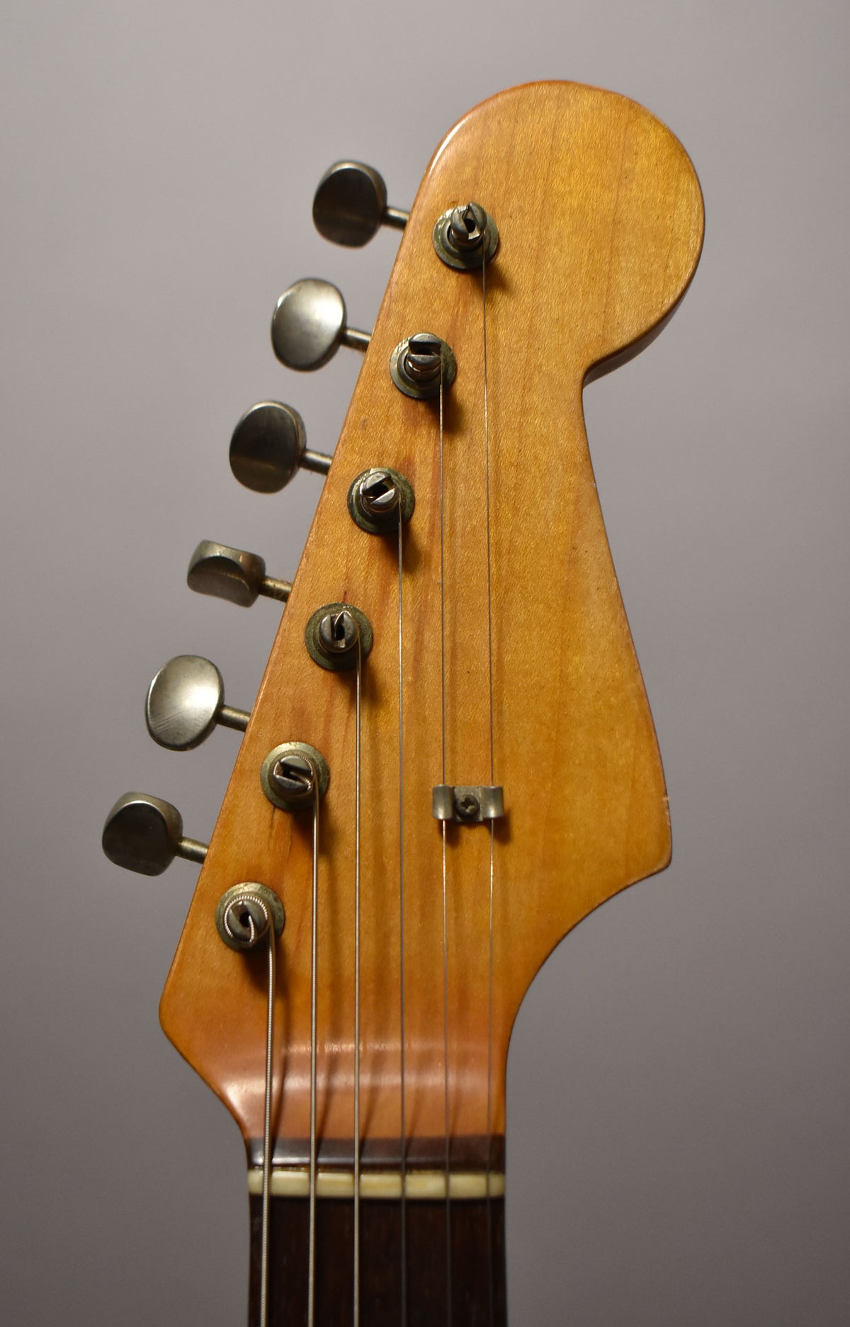 Close-up of the guitar's headstock, showing six tarnished tuners, a string tree, and a dark fretboard with a bone nut.