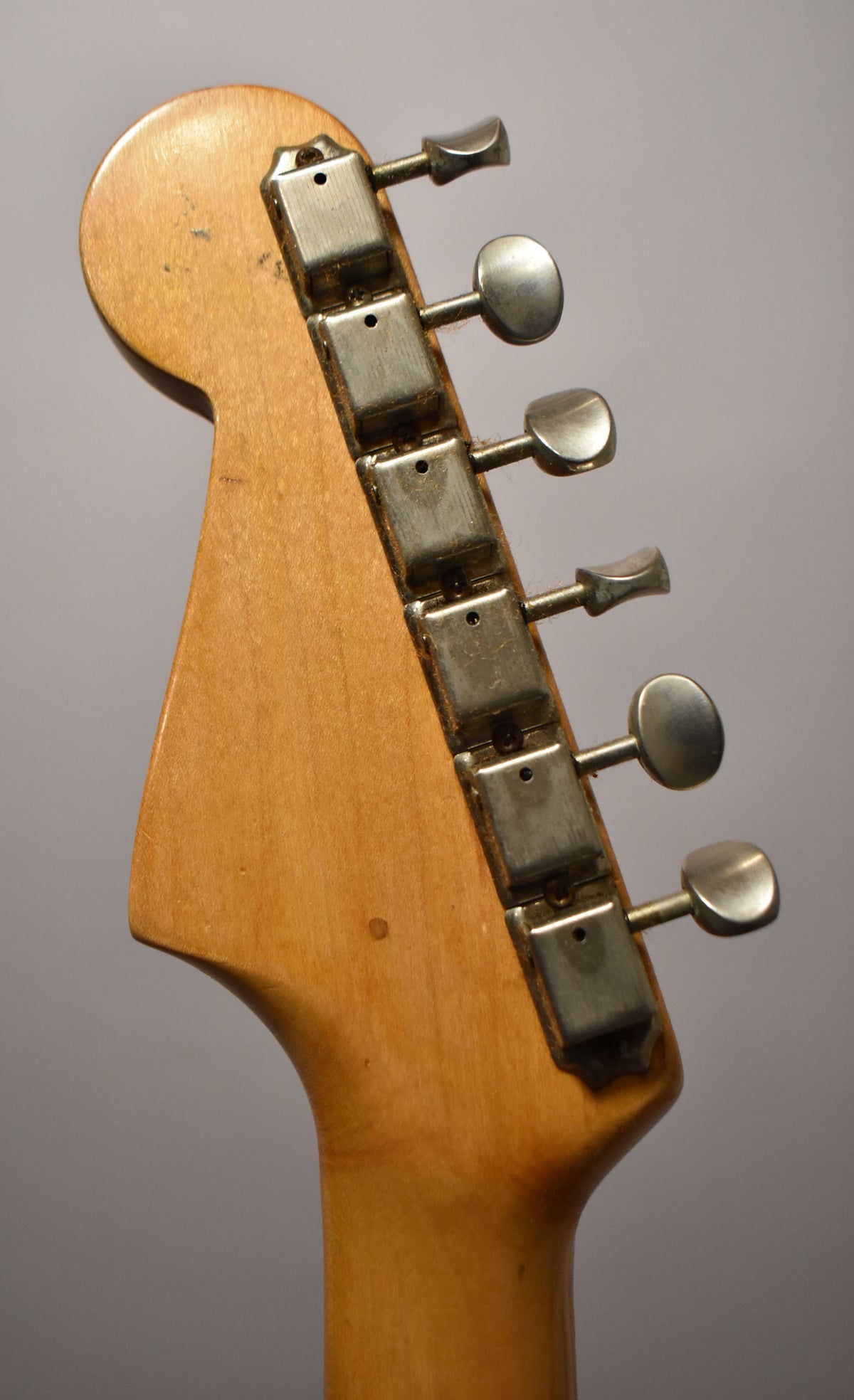 The guitar's headstock and top of the neck, viewed from the back, show six metal tuners with oval buttons and some wear on the wood.