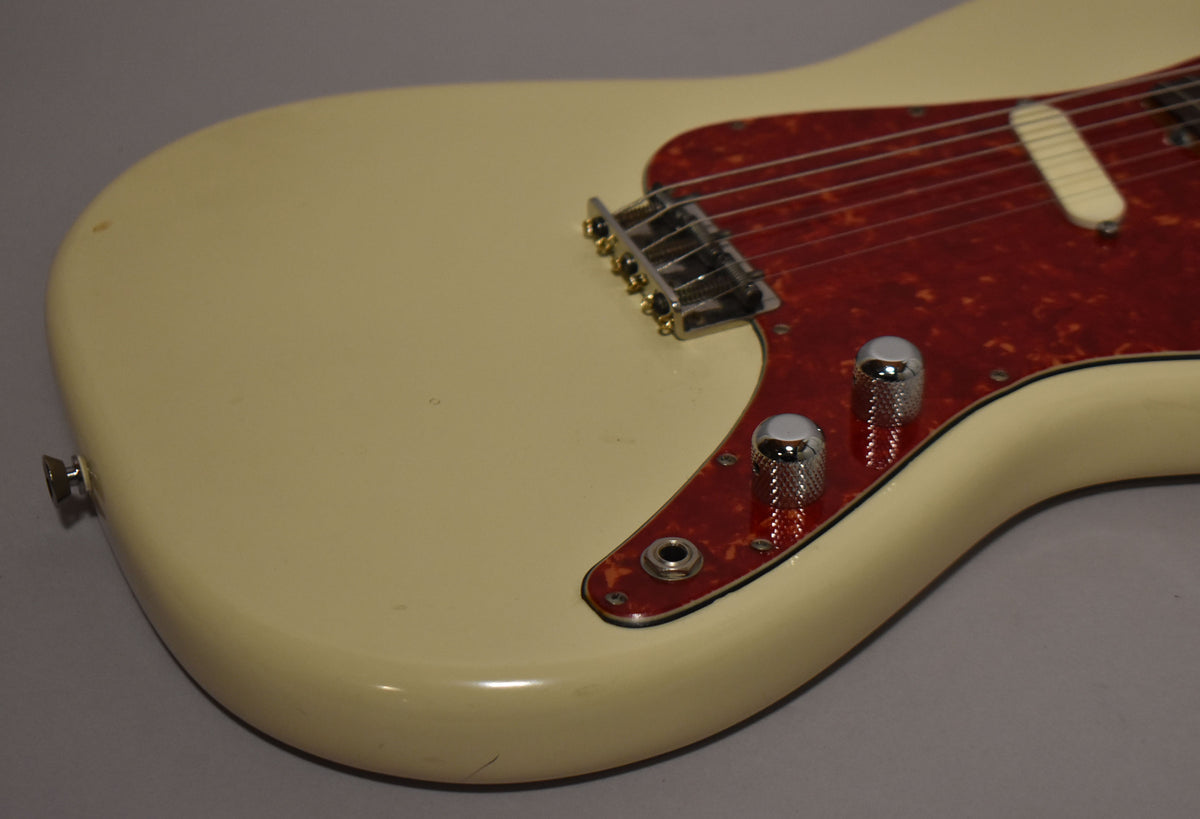 Close-up of the guitar's lower body, showing the aged white finish, tortoise pickguard, chrome bridge, single pickup, and two knurled chrome knobs.