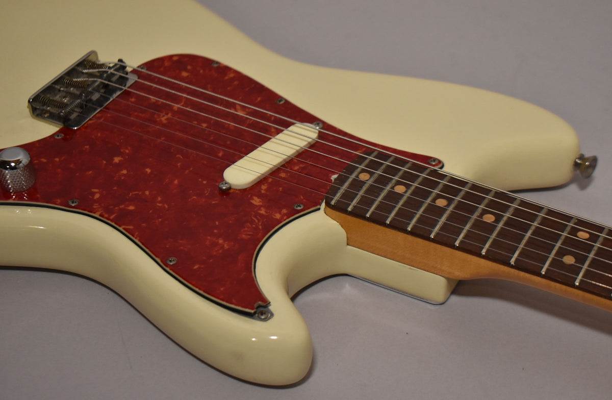 Close-up of a white electric guitar with a red tortoiseshell pickguard, single white pickup, chrome bridge, and dark fretboard.