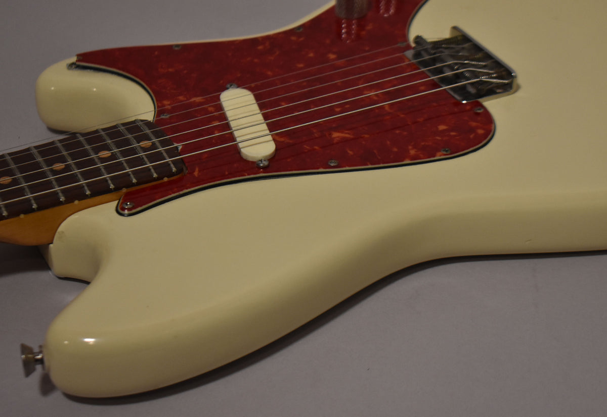 Close-up of the white guitar body, showing the red tortoiseshell pickguard, single cream pickup, and chrome bridge.
