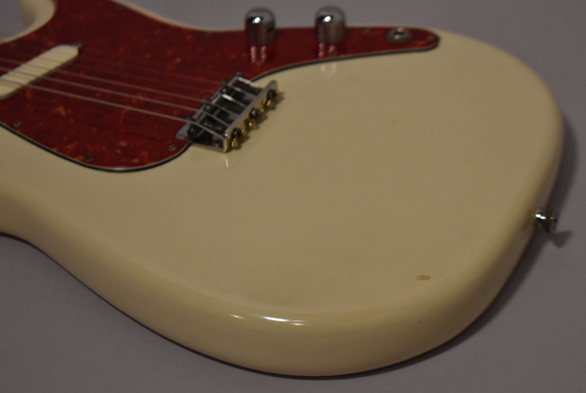 Close-up of the guitar's lower body, showing the white finish, red tortoiseshell pickguard, chrome bridge, and two control knobs.