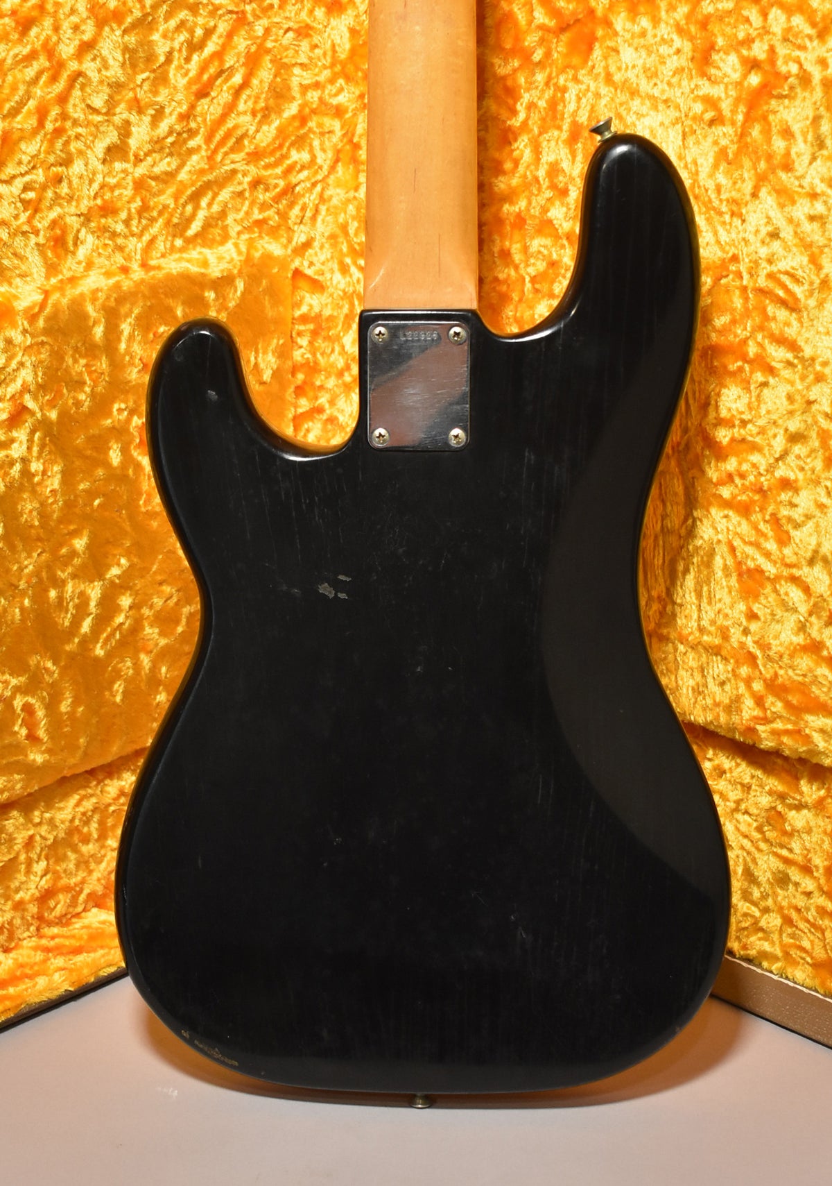 The bass's black body, with visible wear and scratches, is seen from the back, revealing a light wood neck and metal neck plate.