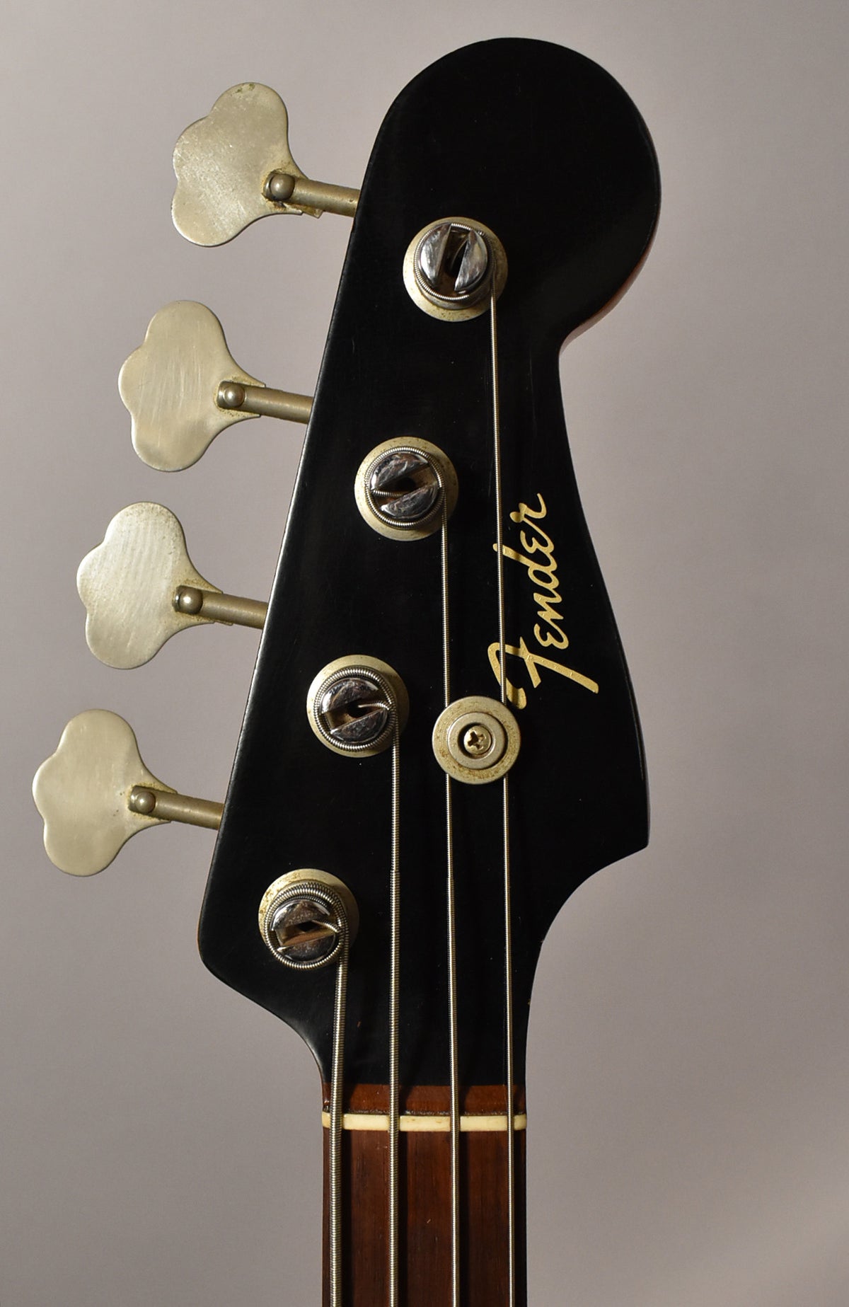 Close-up of the black headstock with gold logo, showing four clover-leaf tuners with tarnished metal paddles and string tree.