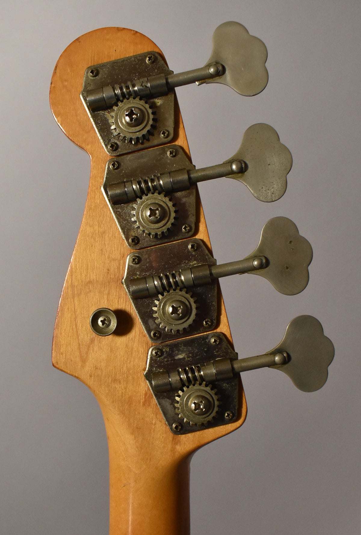 Rear view of the bass headstock, showing four clover-leaf tuners with aged, tarnished metal hardware and a worn maple finish.