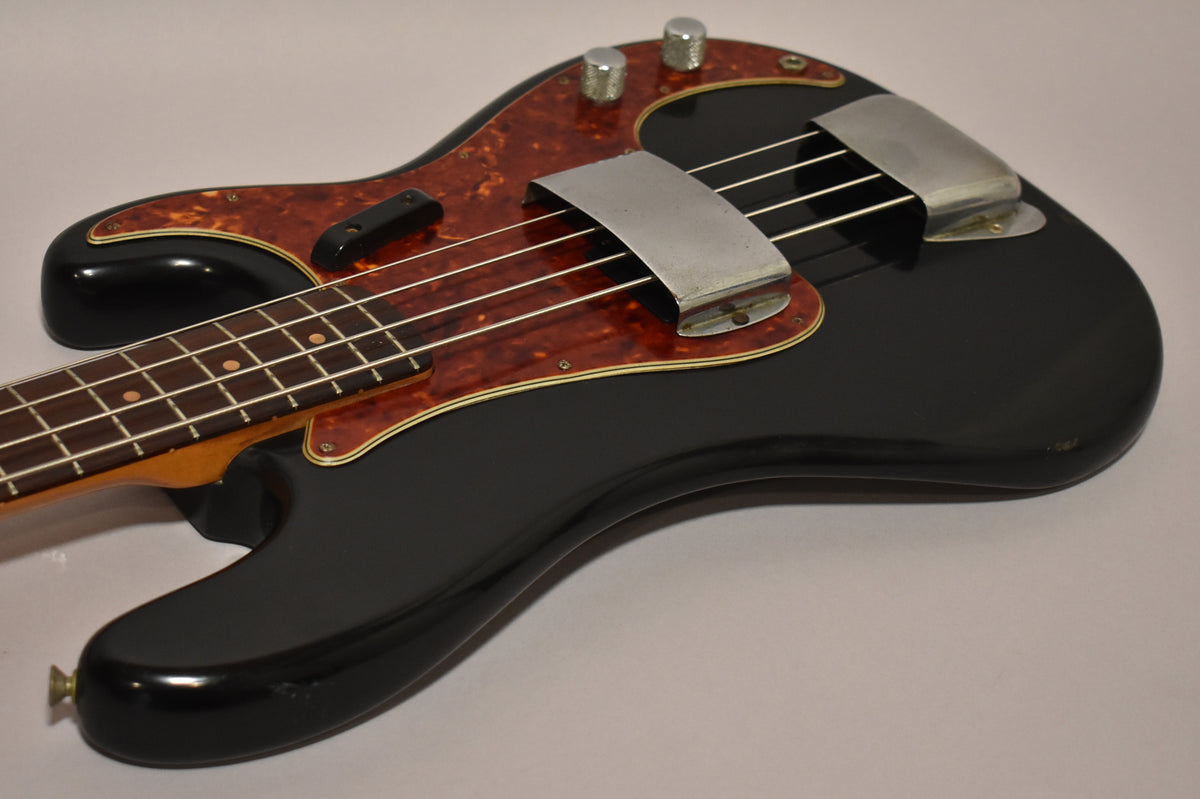 The black bass body, with a tortoiseshell pickguard and chrome covers, is angled from the neck to the lower bout, showing some wear.