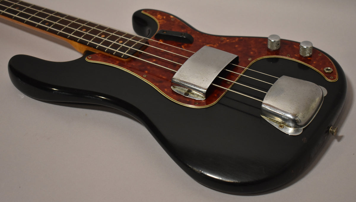 The black bass body and tortoiseshell pickguard are visible from the upper bout, with chrome covers over the pickup and bridge, and two knurled knobs.