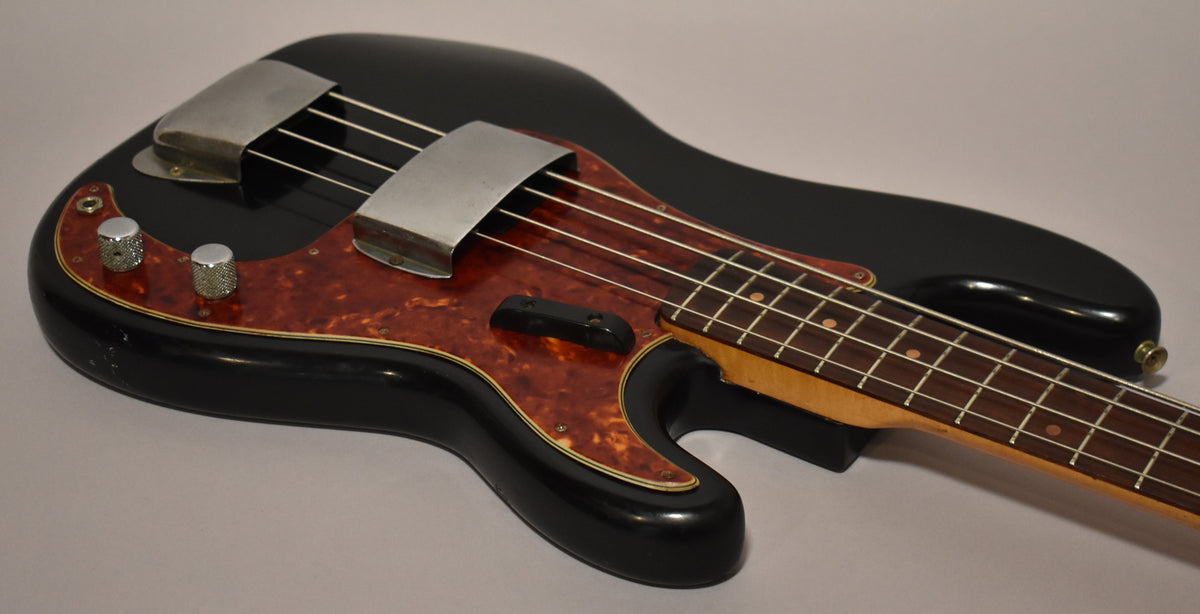A black bass guitar with a tortoiseshell pickguard, chrome bridge and pickup covers, and two knurled chrome knobs.