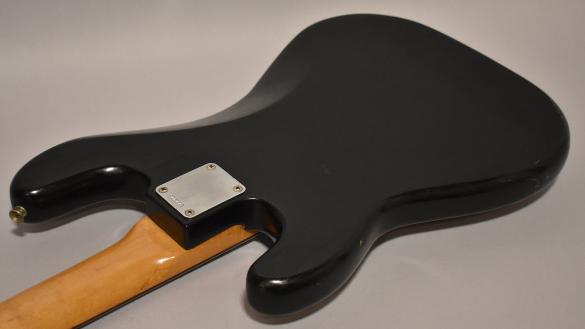 The black refinished bass body is angled from the back, showing the neck plate, strap button, and a few chips and scratches.