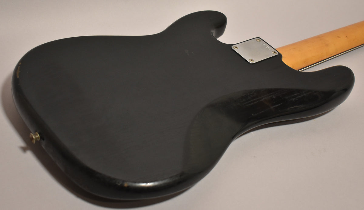 The black bass body, viewed from the back, shows heavy buckle rash and wear along the edges, with a chrome neck plate and maple neck.