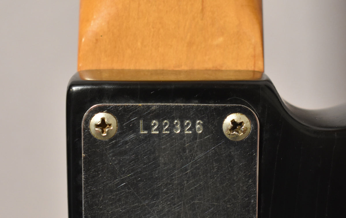 Close-up of the black body's neck plate, showing serial number L22326, two worn screws, and a maple neck heel.