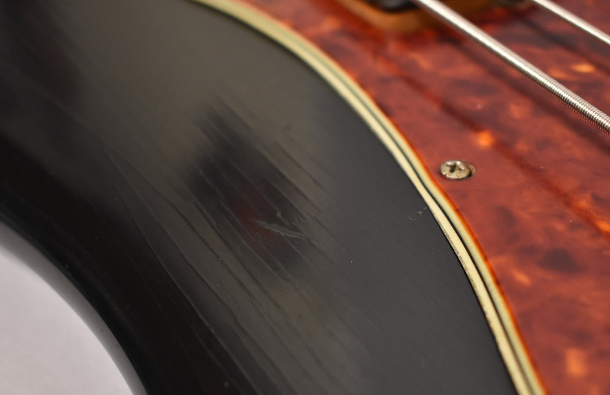 Close-up of a black pickguard with visible scratches, bordered by a thin cream and black line, next to a tortoiseshell pickguard.