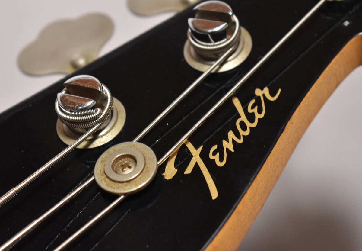 Close-up of the black headstock, showing two chrome tuners with wound strings, a string tree, and a gold logo with some wear.