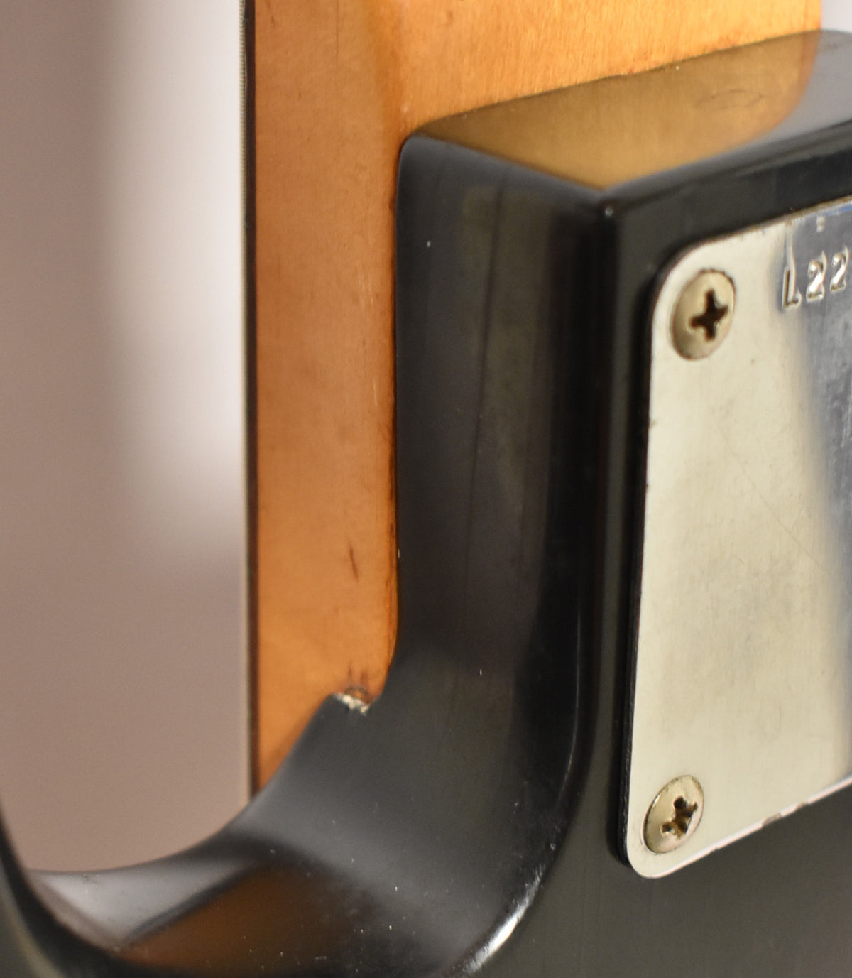 Close-up of the bass's neck heel and body cutaway, showing the black finish, neck plate with screws, and a chip in the wood.