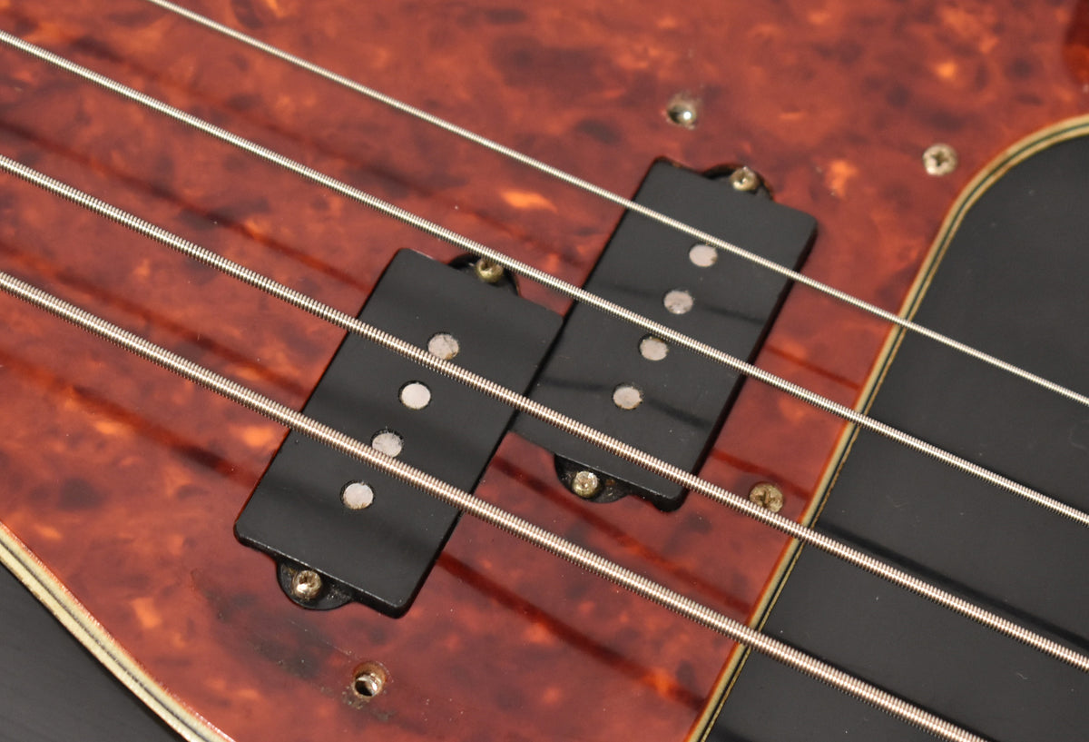 Close-up of the bass's split-coil pickup on a reddish-brown tortoiseshell pickguard, with four strings running over it.
