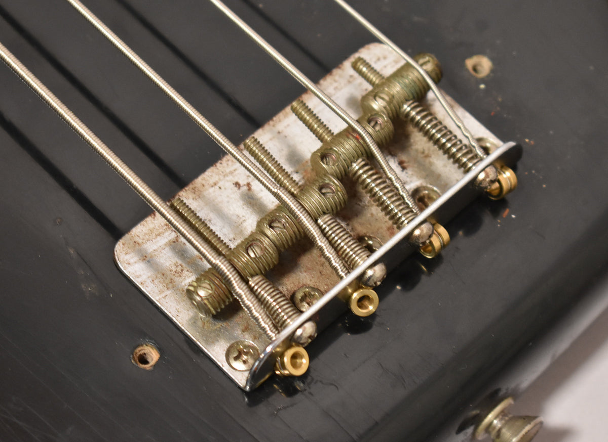 Close-up of the bass's worn, rusty metal bridge and saddles on its black body, with four strings running over them.